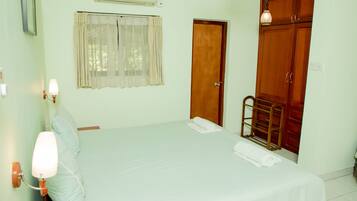 Un dormitorio con cama, mesita de noche, lámpara de pared, ventana con cortinas, armario de madera y puerta.