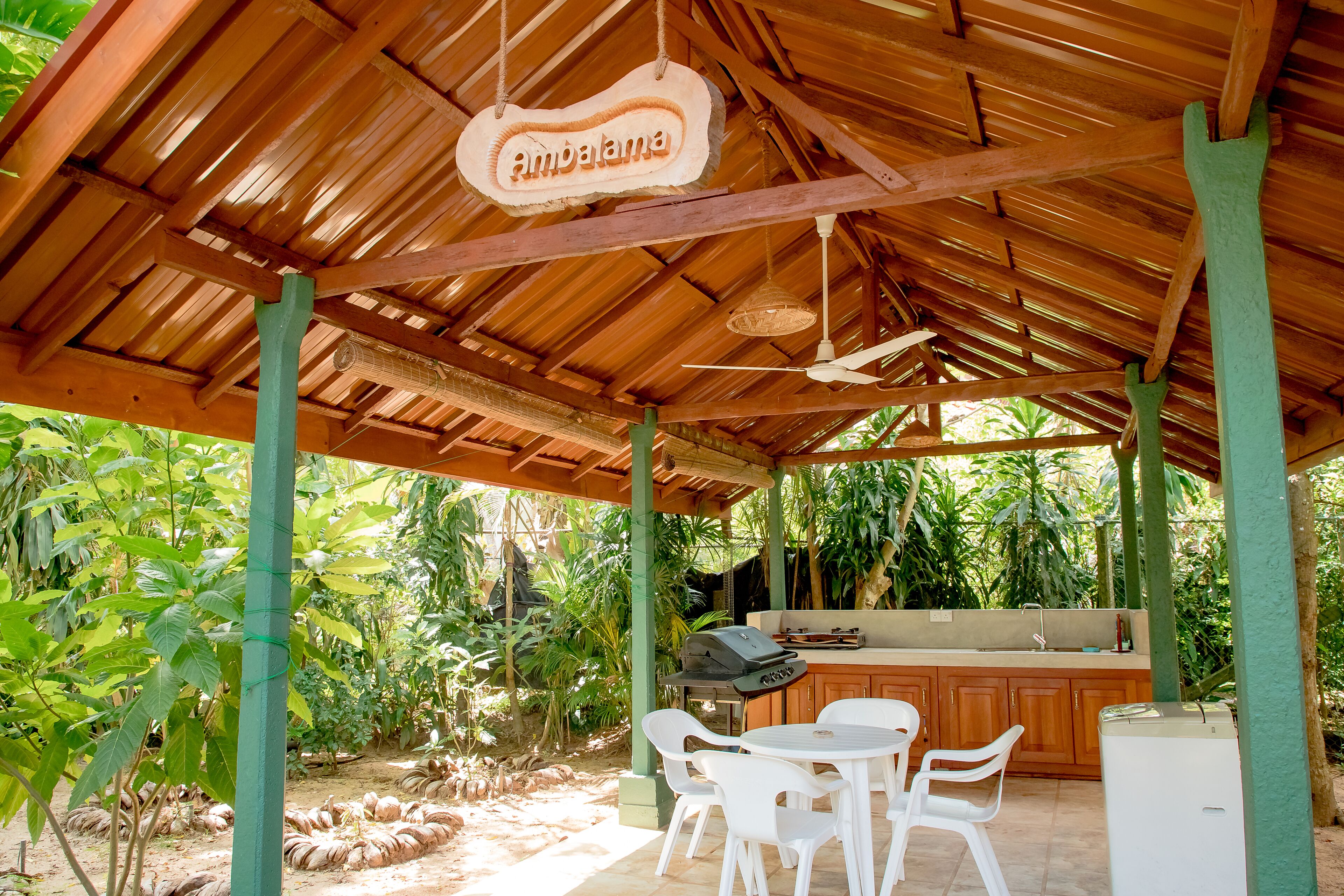 An outdoor covered patio with a wooden ceiling, a grill, white plastic chairs, and a small table.