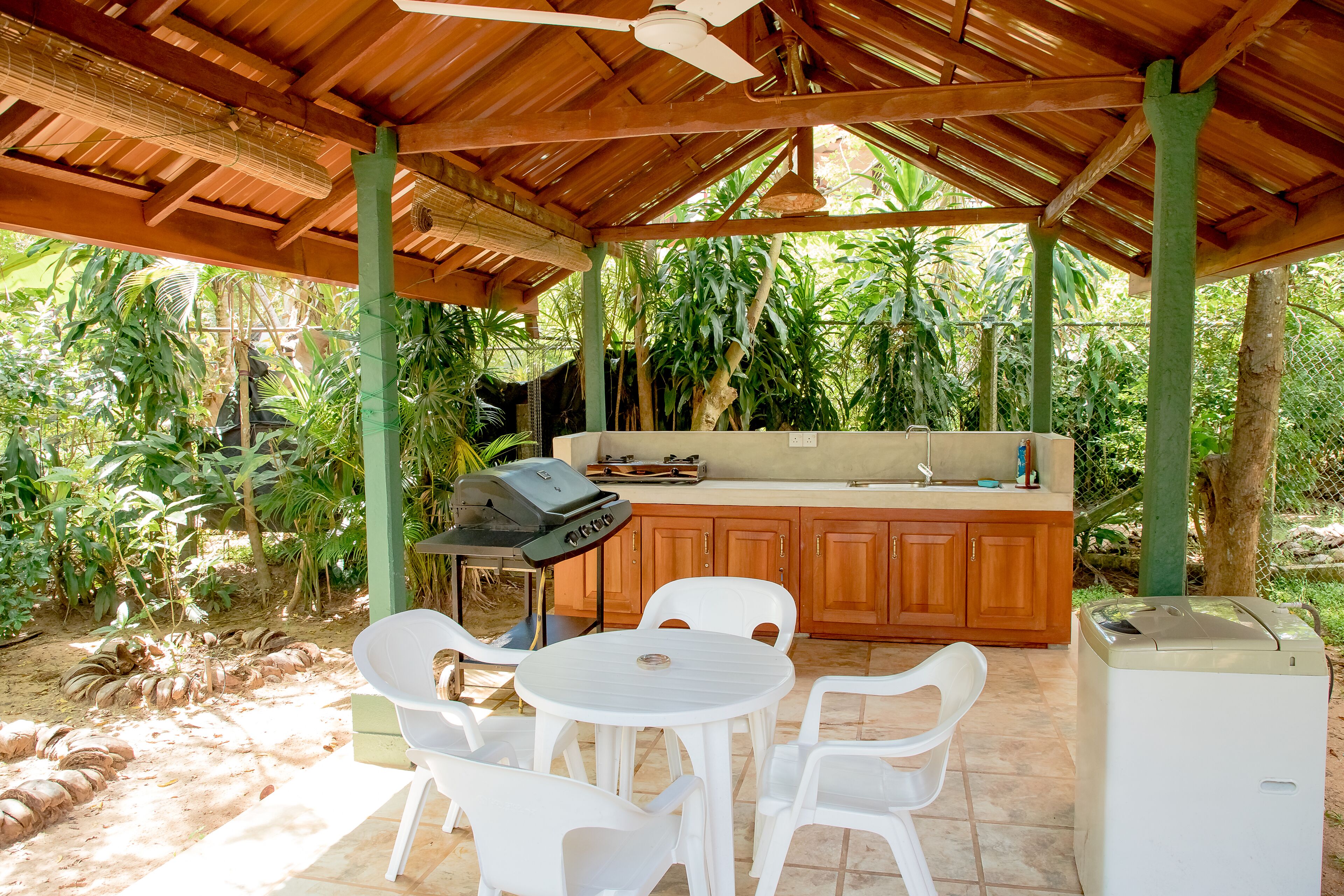 Een terras buiten met houten overkapping, een barbecue, een spoelbak en een wasmachine.