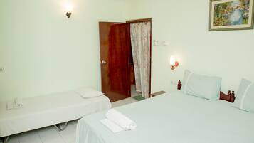 A hotel room with two single beds, a wooden door, a painting on the wall, and a small table with a towel.