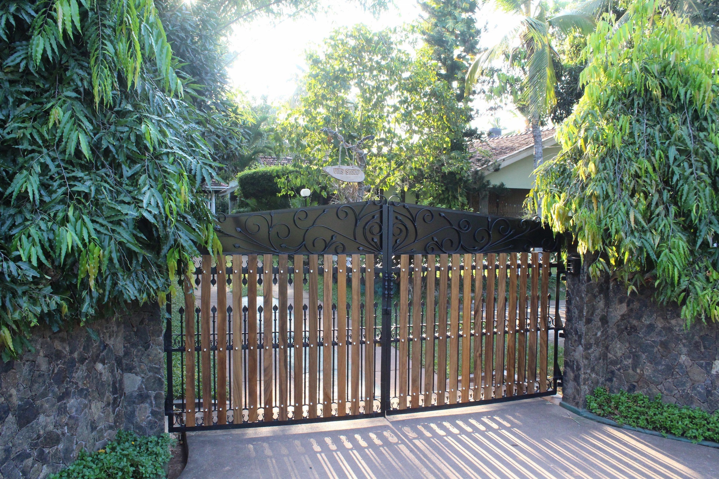 A gated entrance with a stone wall and metal gate, surrounded by lush greenery.