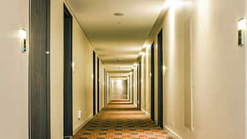 Un couloir d’hôtel avec un tapis à motifs, des portes de chaque côté et un éclairage au plafond.