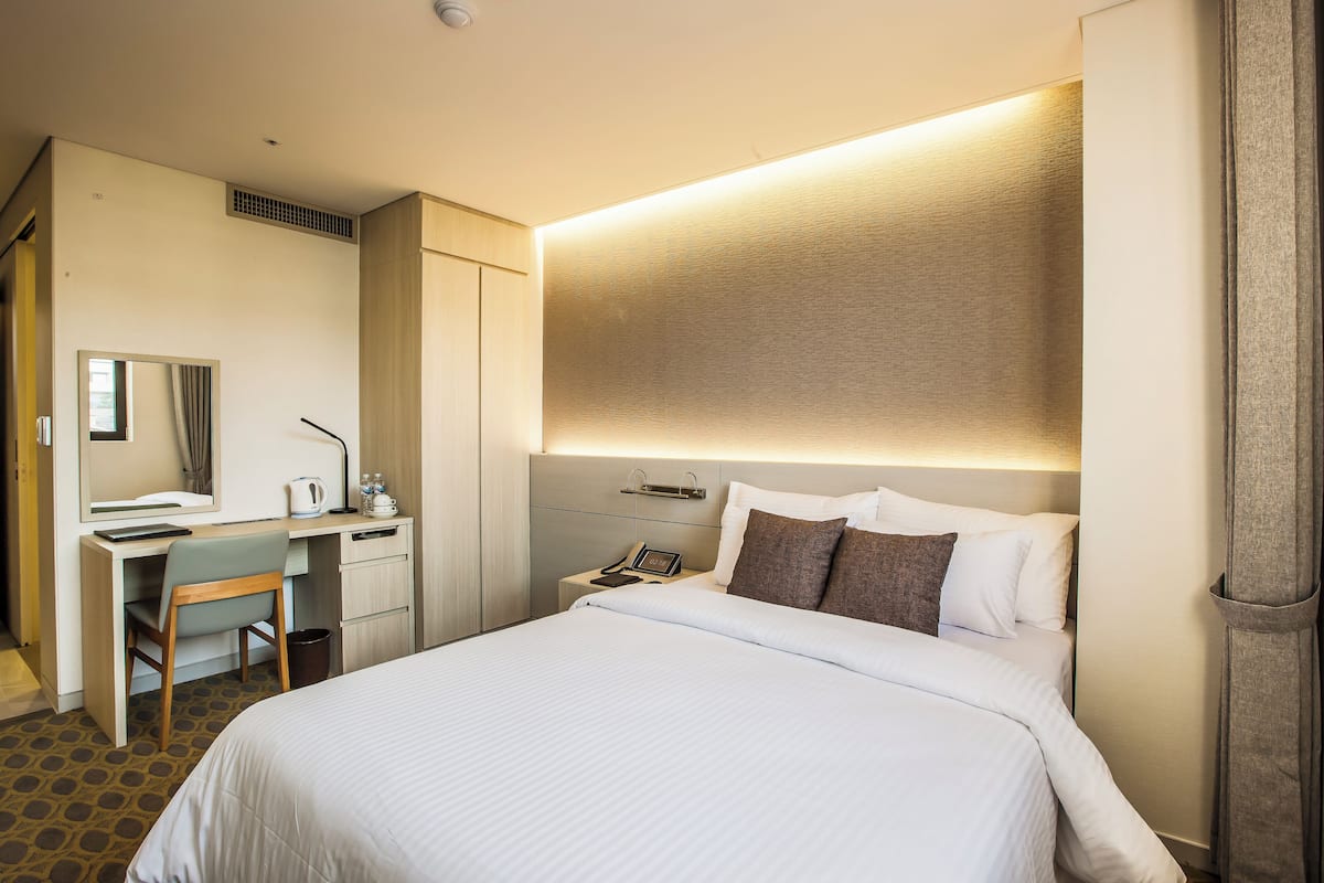 A hotel room with a bed, a desk, a chair, a nightstand, and a mirror.