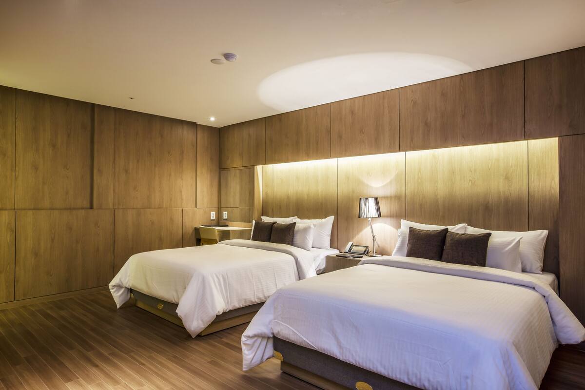 A hotel room with two beds, wooden paneling on the walls, and a modern design.