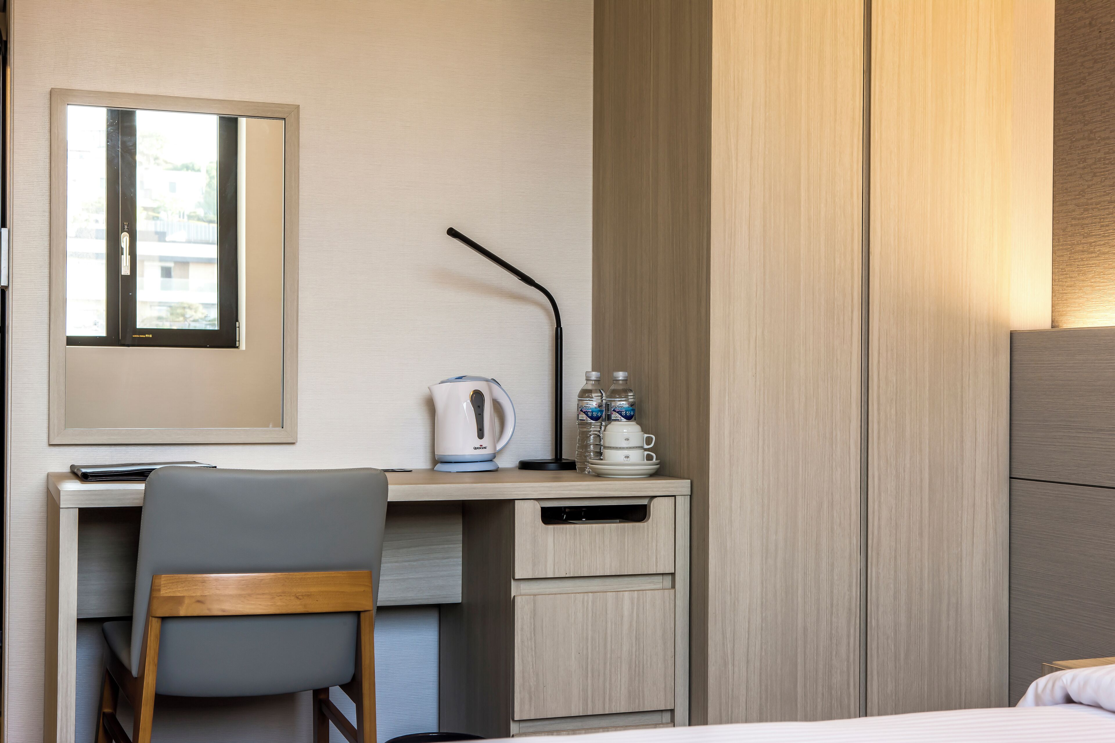 A hotel room with a desk, chair, bed, and a view of buildings outside.