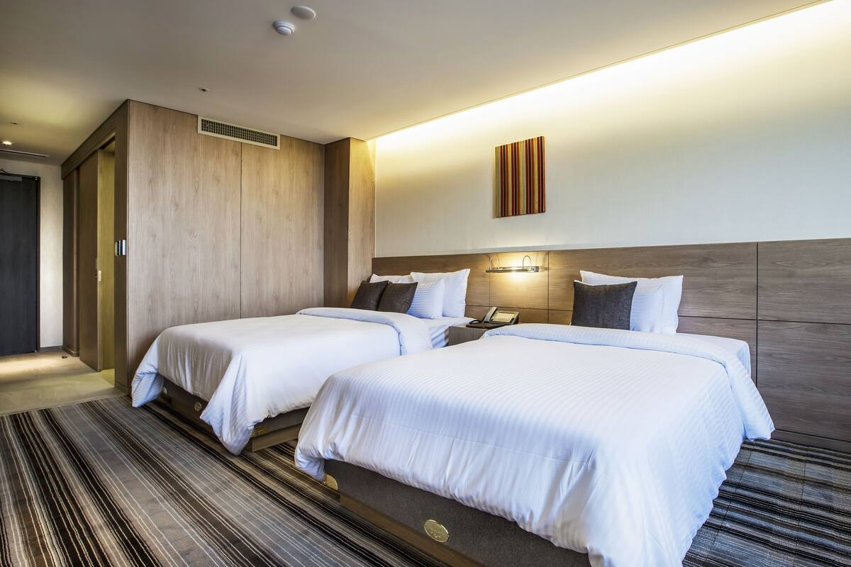 A hotel room with two beds, a wooden headboard, a striped carpet, and a wall-mounted phone.