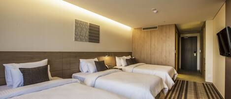 Habitación de hotel con tres camas, cabecera de madera, tapiz decorativo en la pared y televisión montada en la pared.
