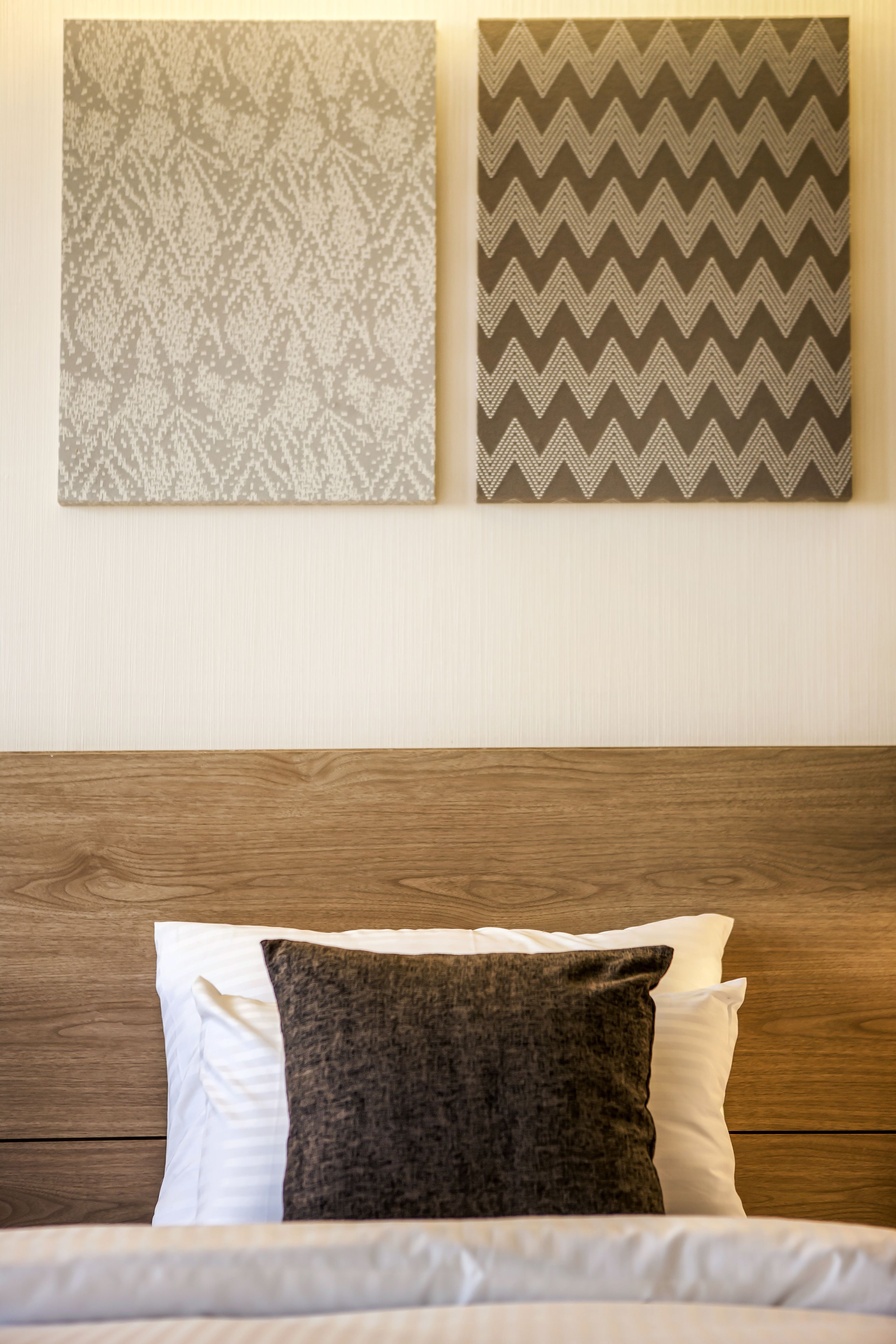 Ein Bett mit weißen und braunen Kissen, einem Holz-Kopfende und zwei gemusterten Wandbehängen darüber.