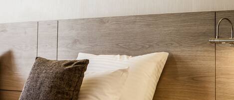 Habitación de hotel con cabecera de madera, cama con ropa blanca, dos almohadas, mesita de noche con teléfono y dos cuadros en la pared.