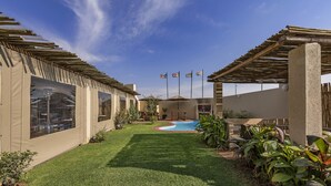 A backyard with a swimming pool, covered patio area, and flags. - Kathu Inn by Country Hotels (Kathu)