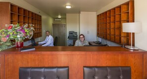 A reception desk with a wooden finish, two leather chairs in front, and a vase of flowers on the left. - Kathu Inn by Country Hotels (Kathu)