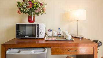 A hotel room with a microwave, a Hisense TV, a small table with a vase of flowers, a lamp, and a coffee maker.