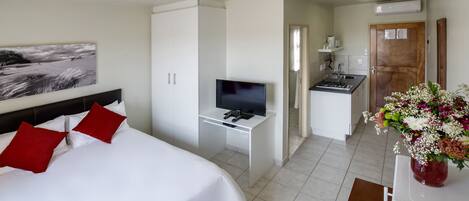 A hotel room with a bed, a TV, a kitchenette, and a bathroom.