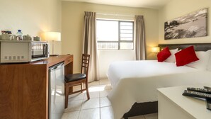 A hotel room with a bed, a desk with a microwave, a chair, a TV, and a window with curtains. - Kathu Inn by Country Hotels (Kathu)