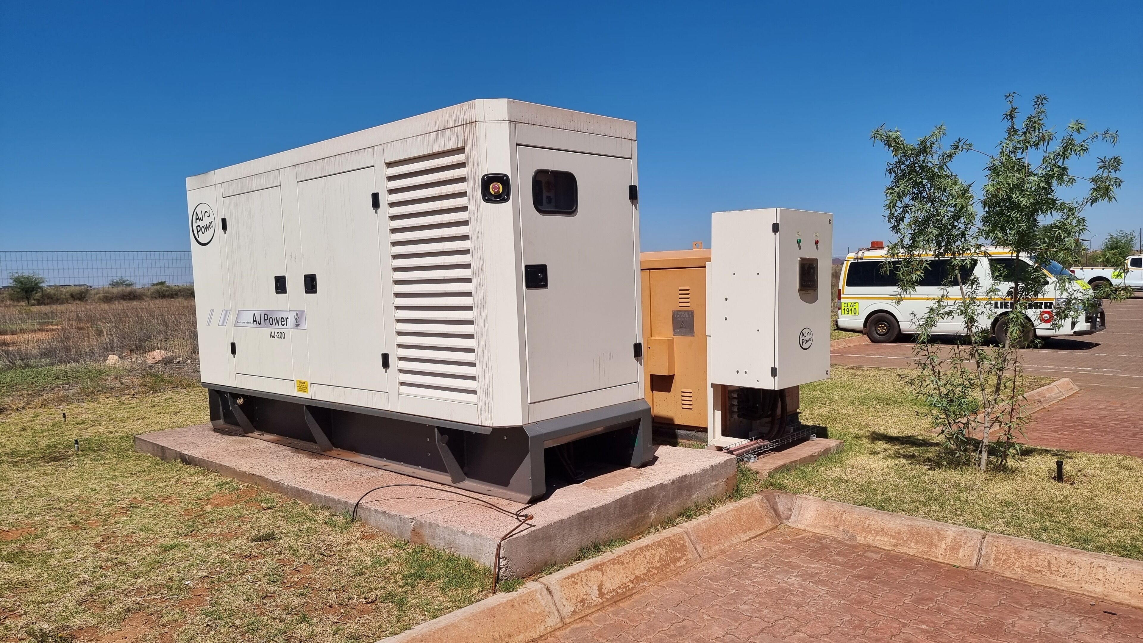A utility transformer with a label 'AJ Power' and model 'AI-200' in a grassy area with a parked vehicle in the background.
