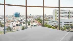 Une vue sur la ville, encadrée par de grandes fenêtres, qui présente un mélange de bâtiments résidentiels et commerciaux, dont un immeuble Vinicil particulièrement remarquable.