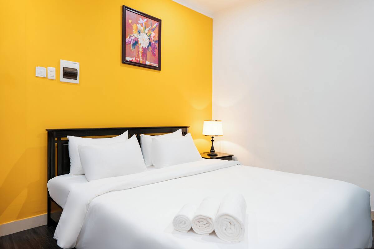 A hotel room with a bed, a nightstand, a lamp, and a painting on the wall.