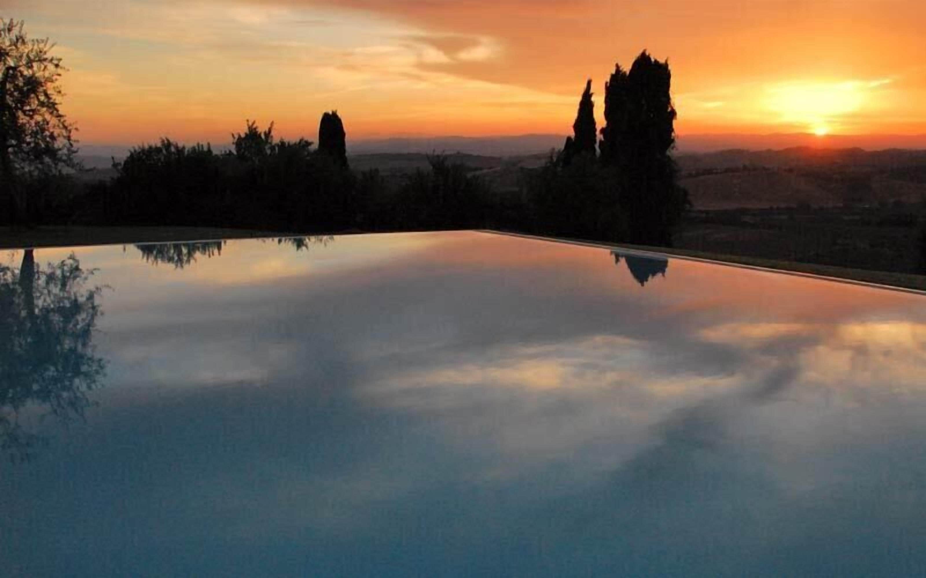 A serene sunset over a reflective pool with distant trees and a clear sky.