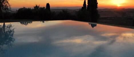 A serene sunset over a reflective pool with distant trees and a clear sky.