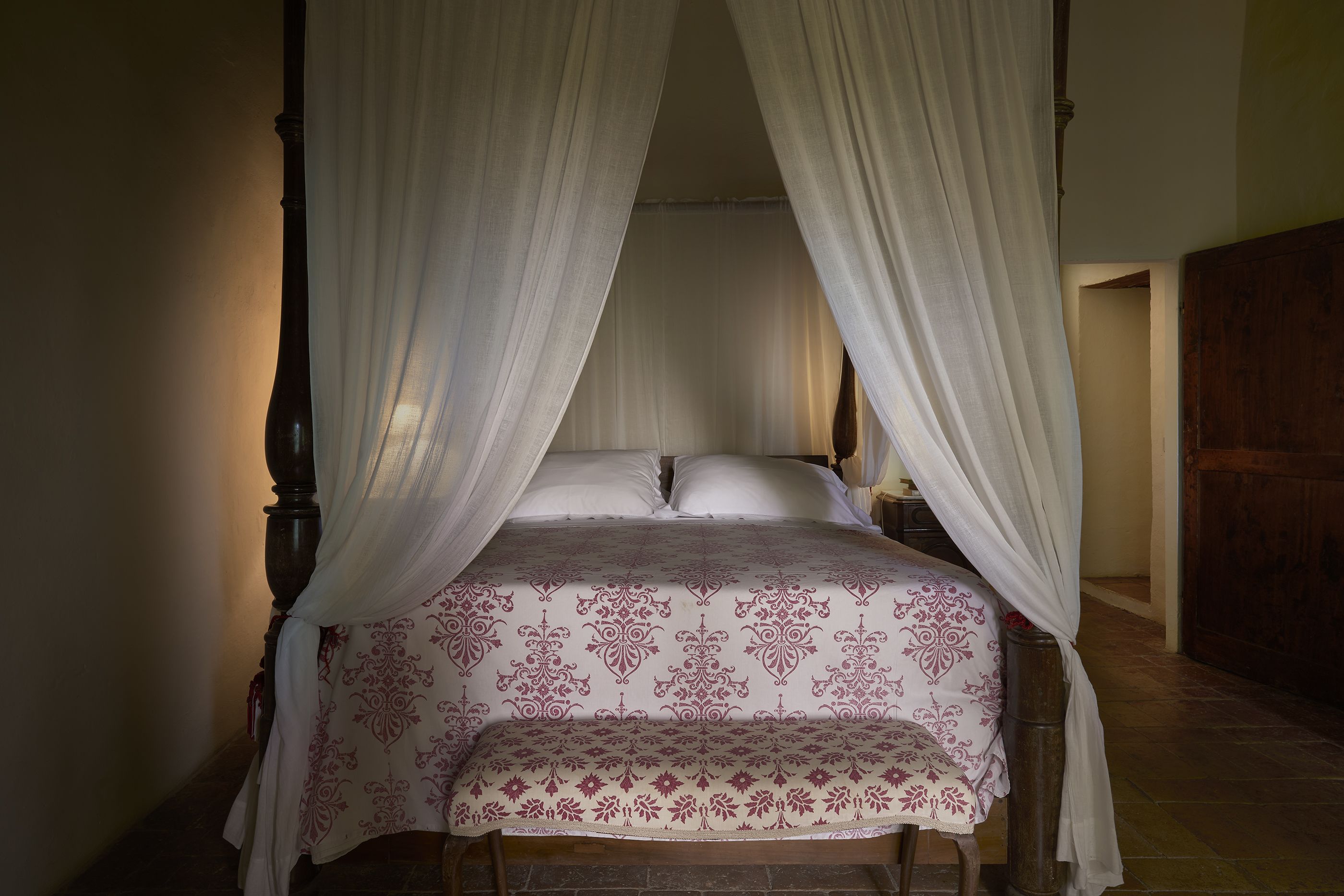 A four-poster bed with a canopy, a wooden headboard, and a bench at the foot of the bed.