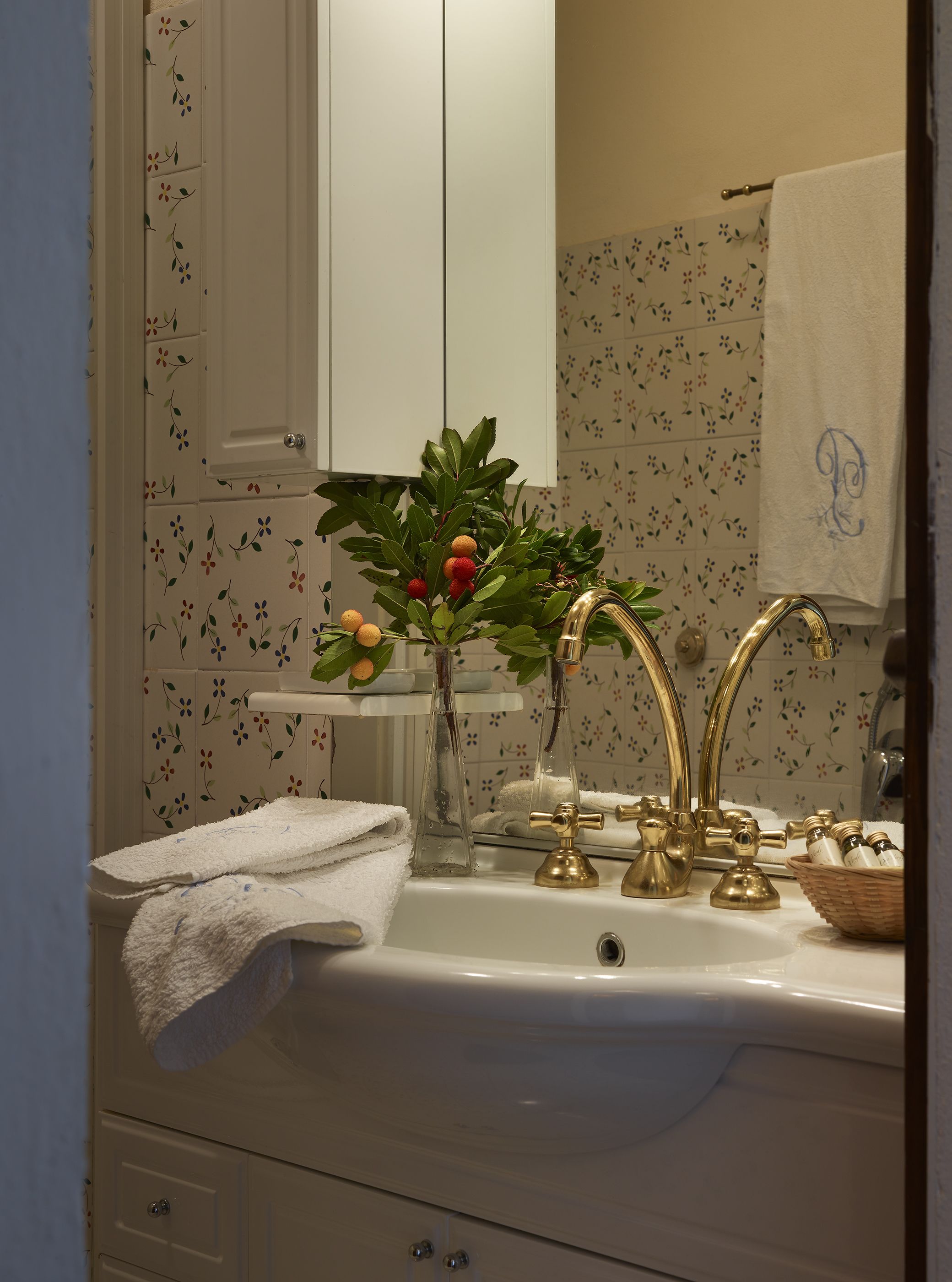 Une salle de bain avec un lavabo blanc, des robinets dorés et un miroir. Une serviette est accrochée au mur et un panier contenant des articles de toilette est posé sur le comptoir.