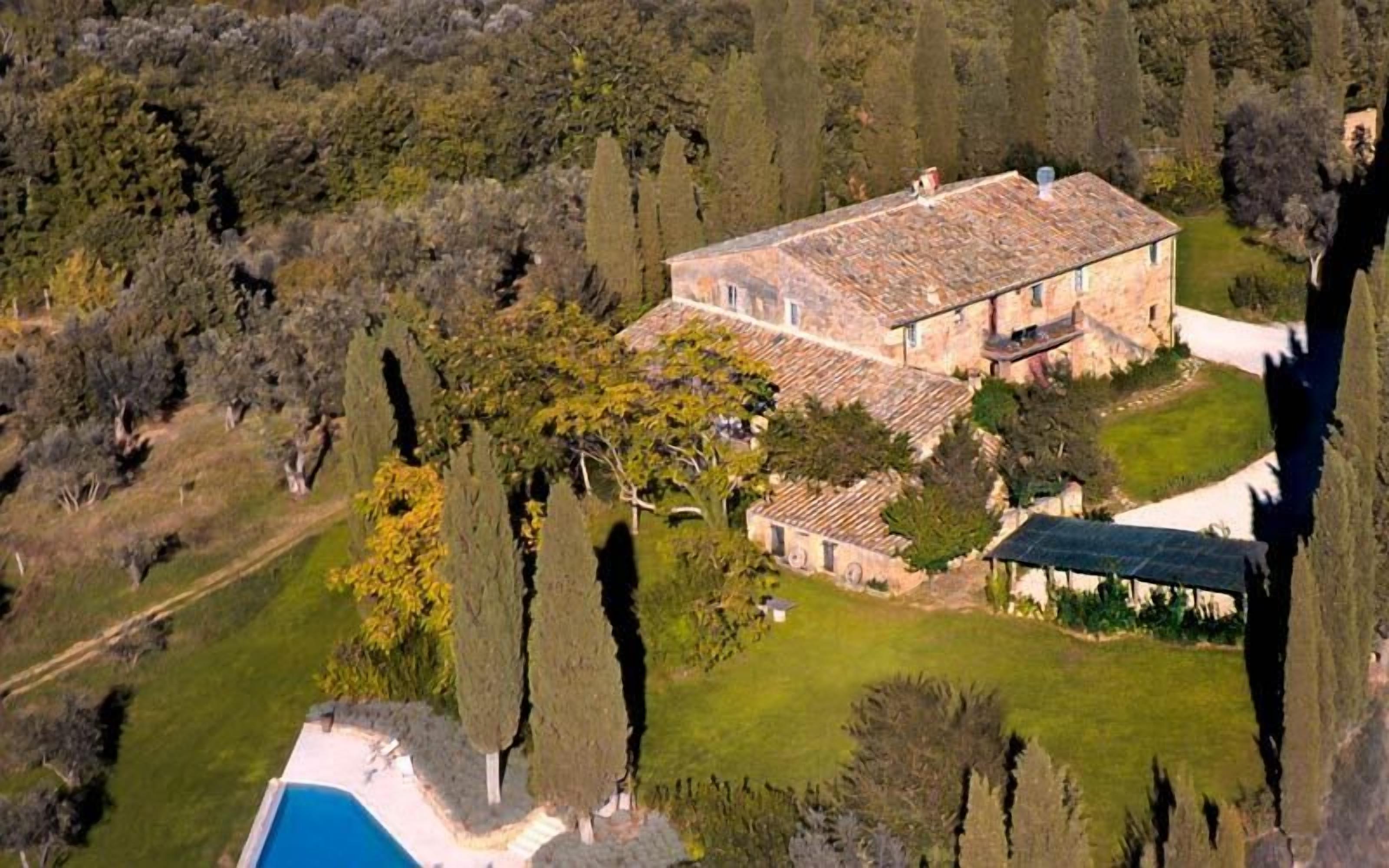 An aerial view of a large house with a tiled roof, surrounded by trees and a swimming pool.