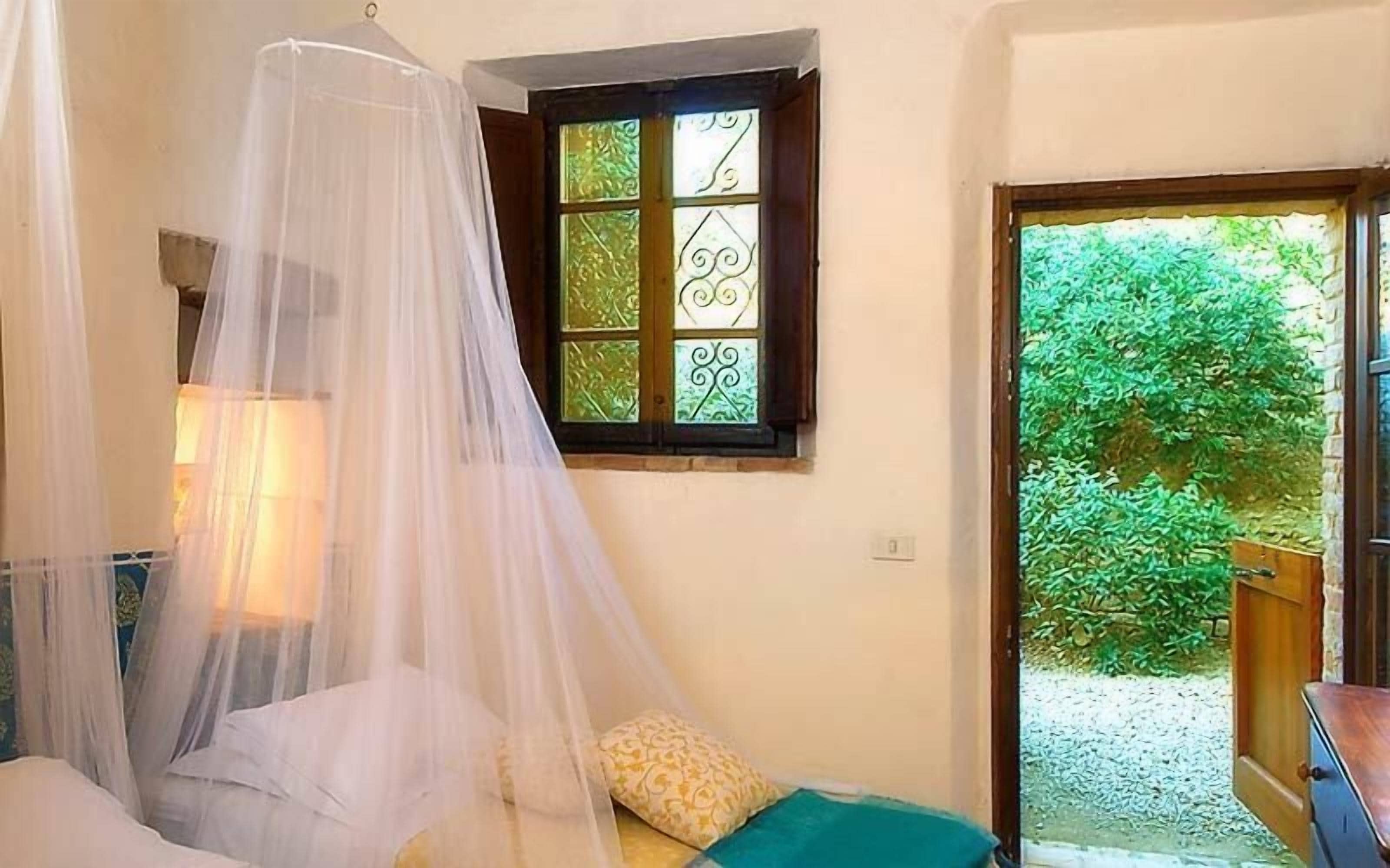Une chambre à coucher avec un lit à baldaquin, une fenêtre ornée de vitraux décoratifs et une vue sur la verdure environnante.