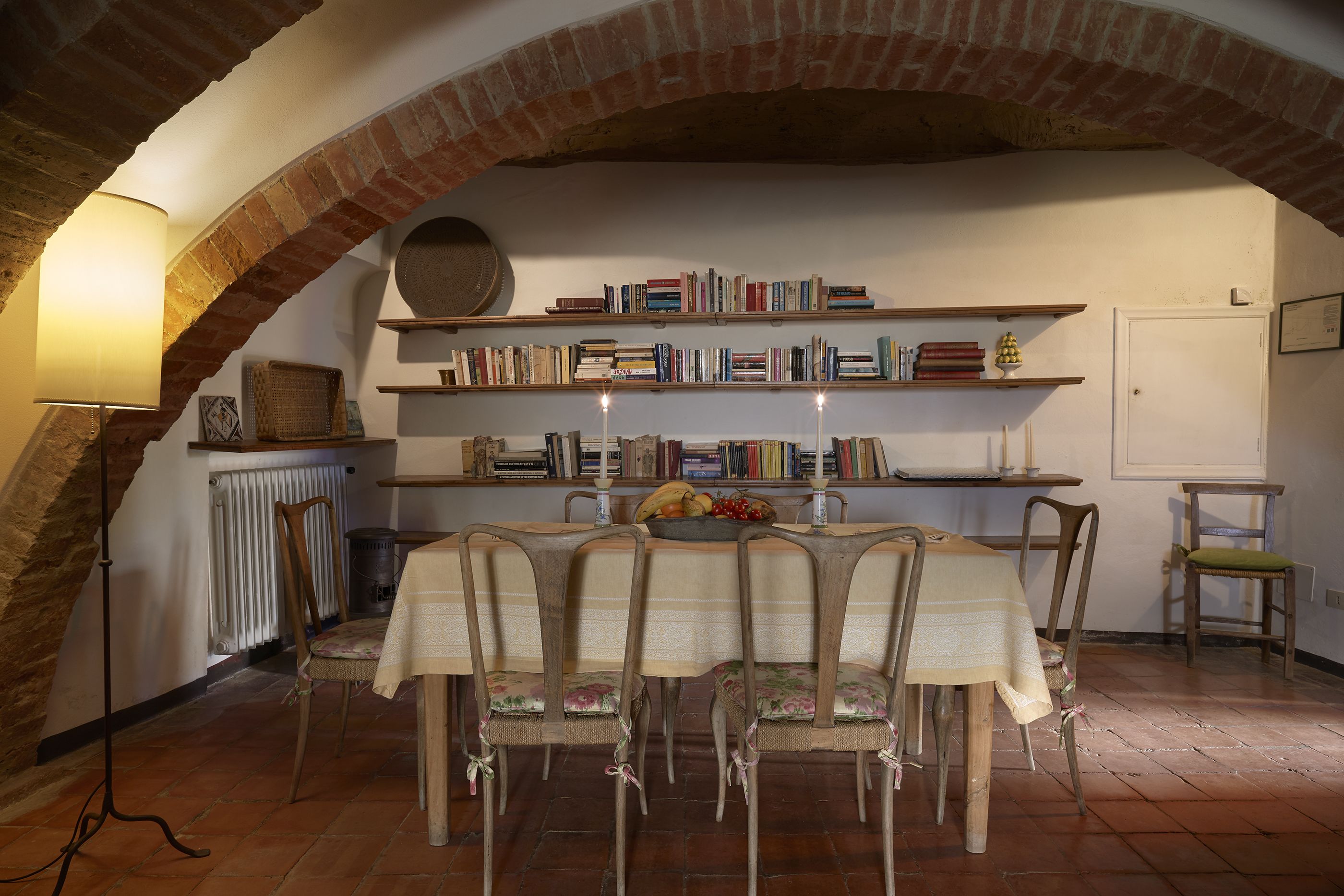 Comedor con arco de ladrillo, una mesa con sillas, una estantería y un radiador.