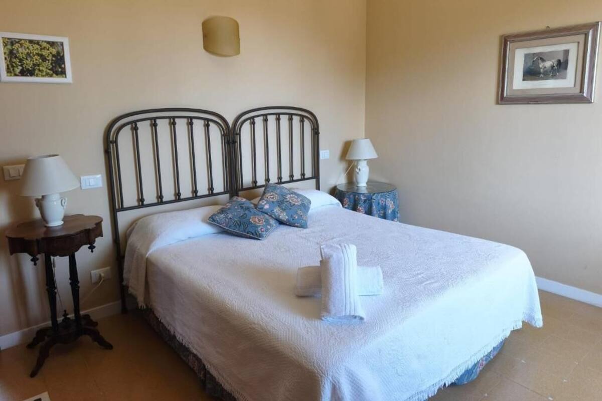 A bedroom with a bed, two bedside tables, a wall-mounted lamp, and a framed picture.