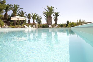 A clear swimming pool with lounge chairs and umbrellas, surrounded by palm trees and a stone building. - Agriturismo Baglio Vecchio (Castelvetrano)
