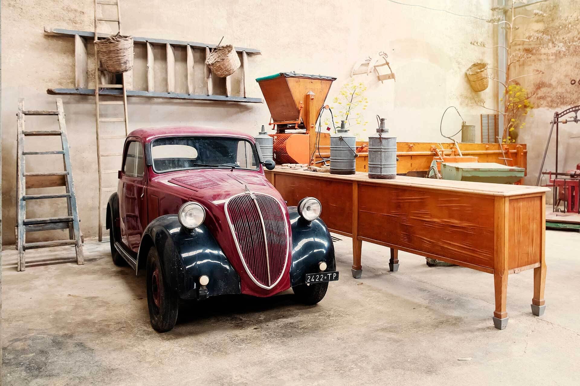 A vintage car parked in a garage with a wooden desk and various tools.