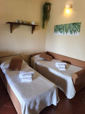 Two single beds with towels, a shelf with small containers, a wall-mounted plant, and a wall-mounted light fixture. - Agriturismo Baglio Vecchio (Castelvetrano)