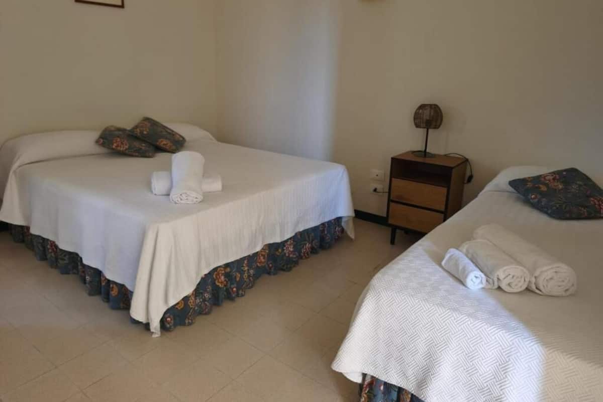 Two single beds with white linens, a small wooden nightstand with a lamp, and a wall-mounted light fixture.
