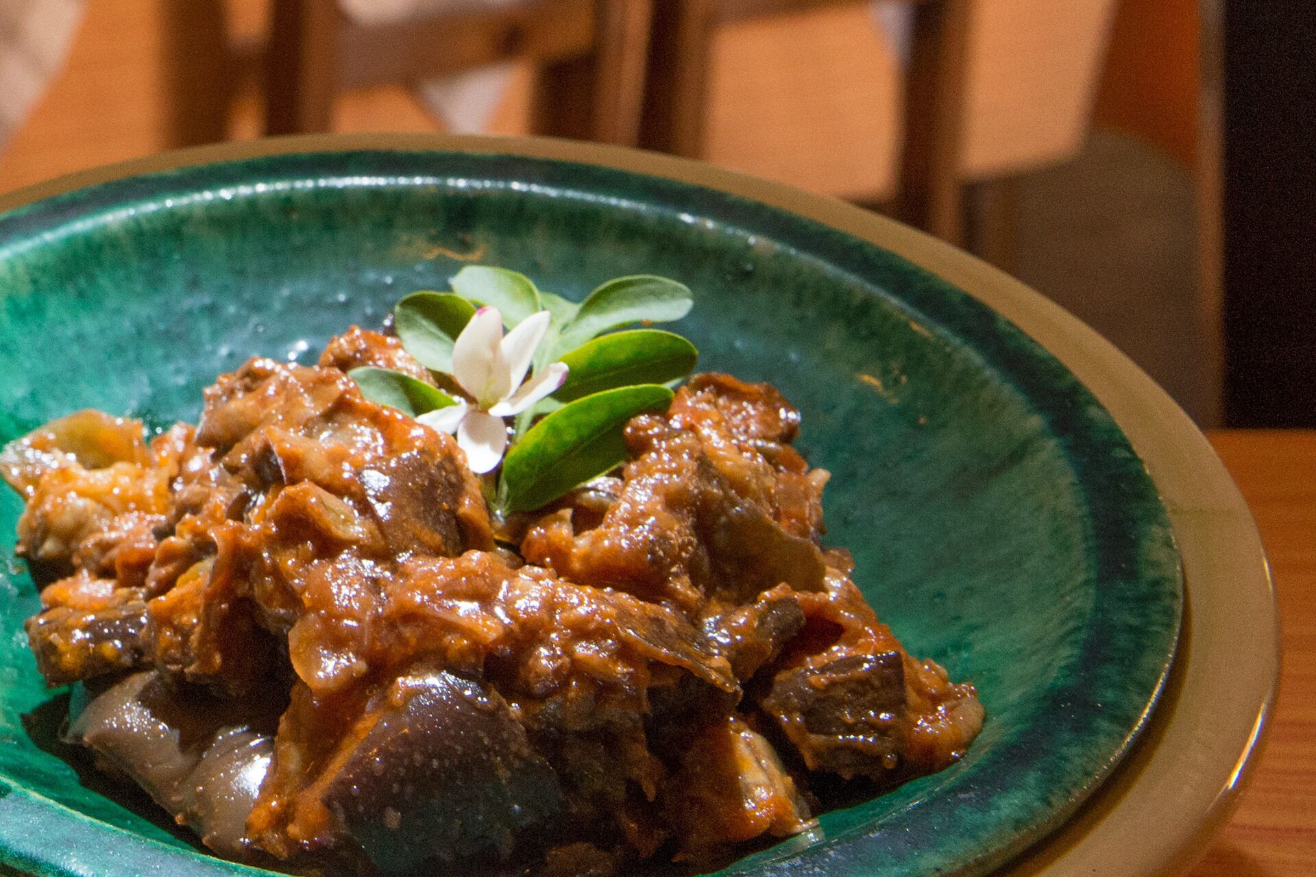 A plate of food with a green rim, possibly a stew or curry, garnished with a white flower.