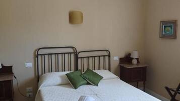 A single bed with a white bedspread and two green pillows, a bedside table with a lamp, and a wall-mounted light fixture.