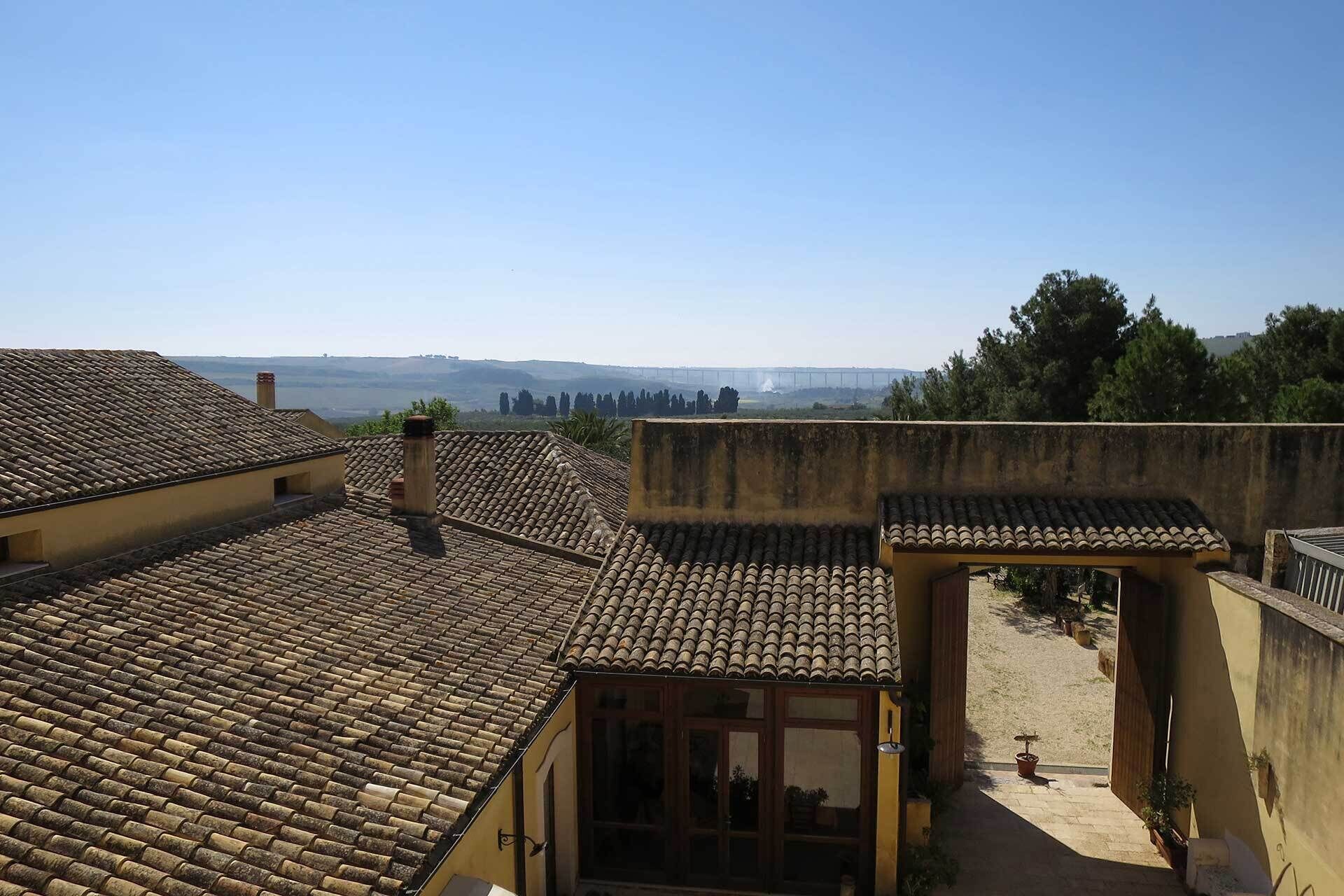 Eine Dachterrasse mit Terrakotta-Fliesen, ein kleiner überdachter Bereich mit einer Holztür und Blick auf ferne Hügel.