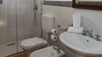 A bathroom with a glass shower enclosure, a toilet, a bidet, a sink, and a mirror.