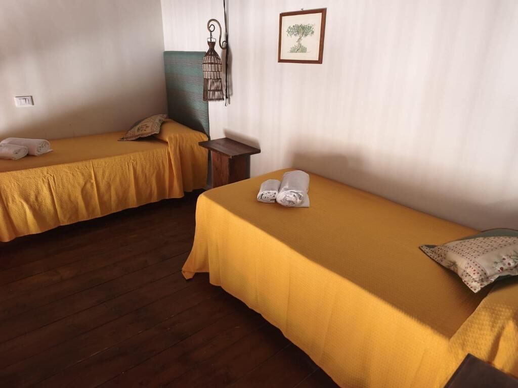 Two single beds with yellow bedding, a small wooden nightstand, a wall-mounted lamp, and a framed picture.