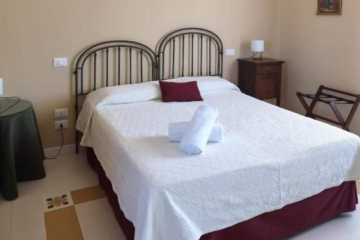 A hotel room with a bed, a nightstand, a chair, and a painting on the wall.