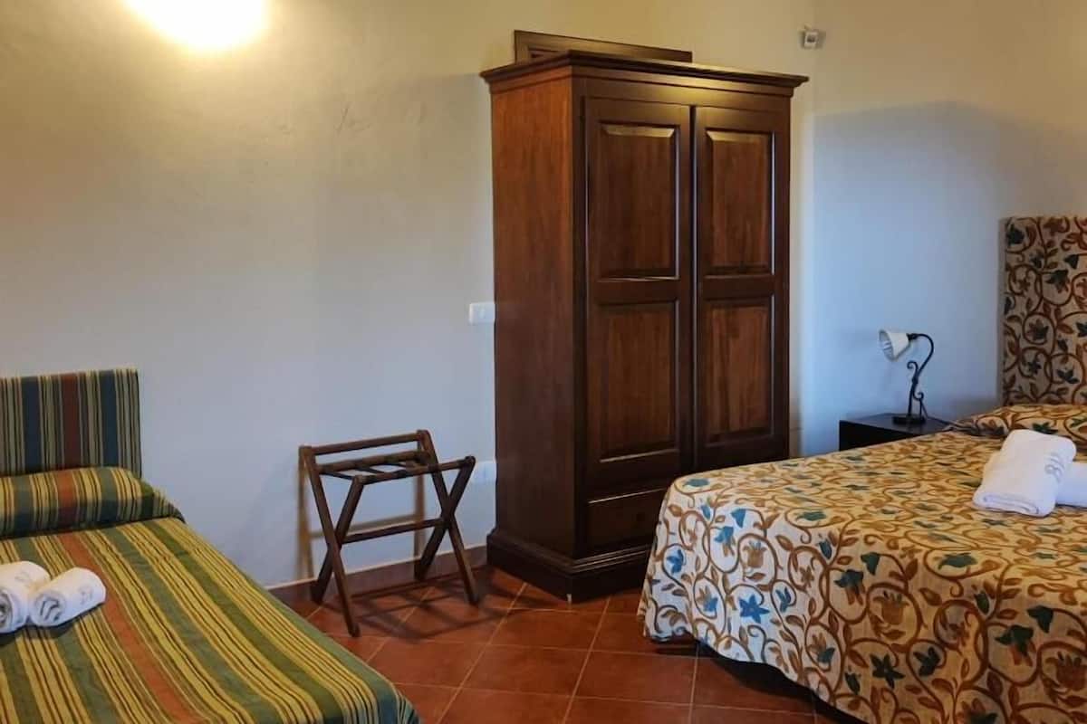 A room with two beds, a wooden wardrobe, a small chair, and a nightstand with a lamp.