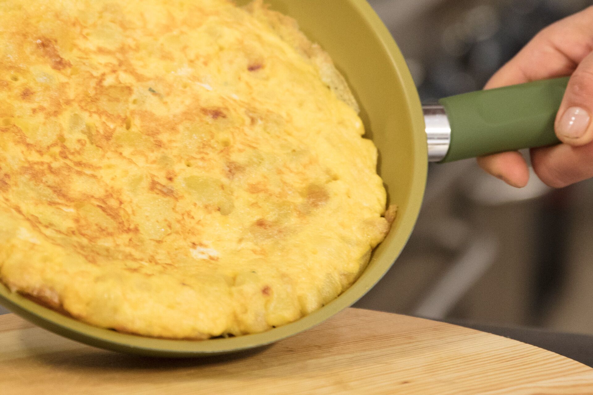A person holding a pan with a cooked omelette.
