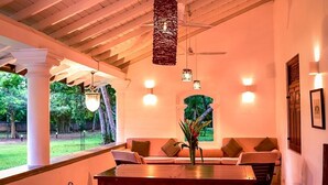 A dining area with a long table, several chairs, hanging lights, and a ceiling fan. - Dansala Cottage (Koggala)