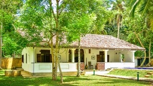 A white building with a tiled roof, surrounded by lush greenery and trees. - Dansala Cottage (Koggala)