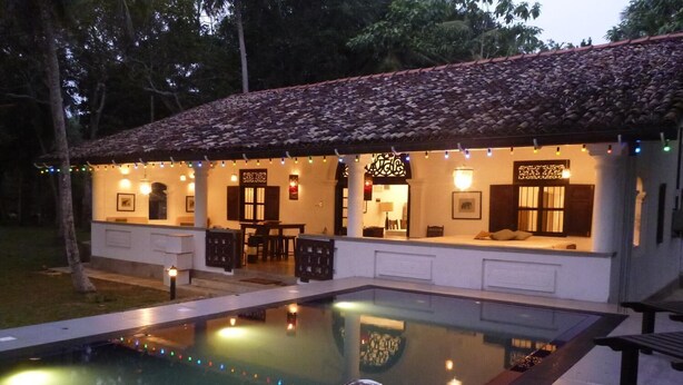 A poolside area with a tiled roof, a pool, and a seating area with a table and chairs. - Dansala Cottage (Koggala)