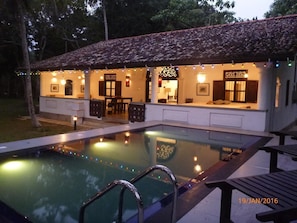 Zona junto a la piscina con techo de azulejos, piscina y área de estar con mesa y sillas.