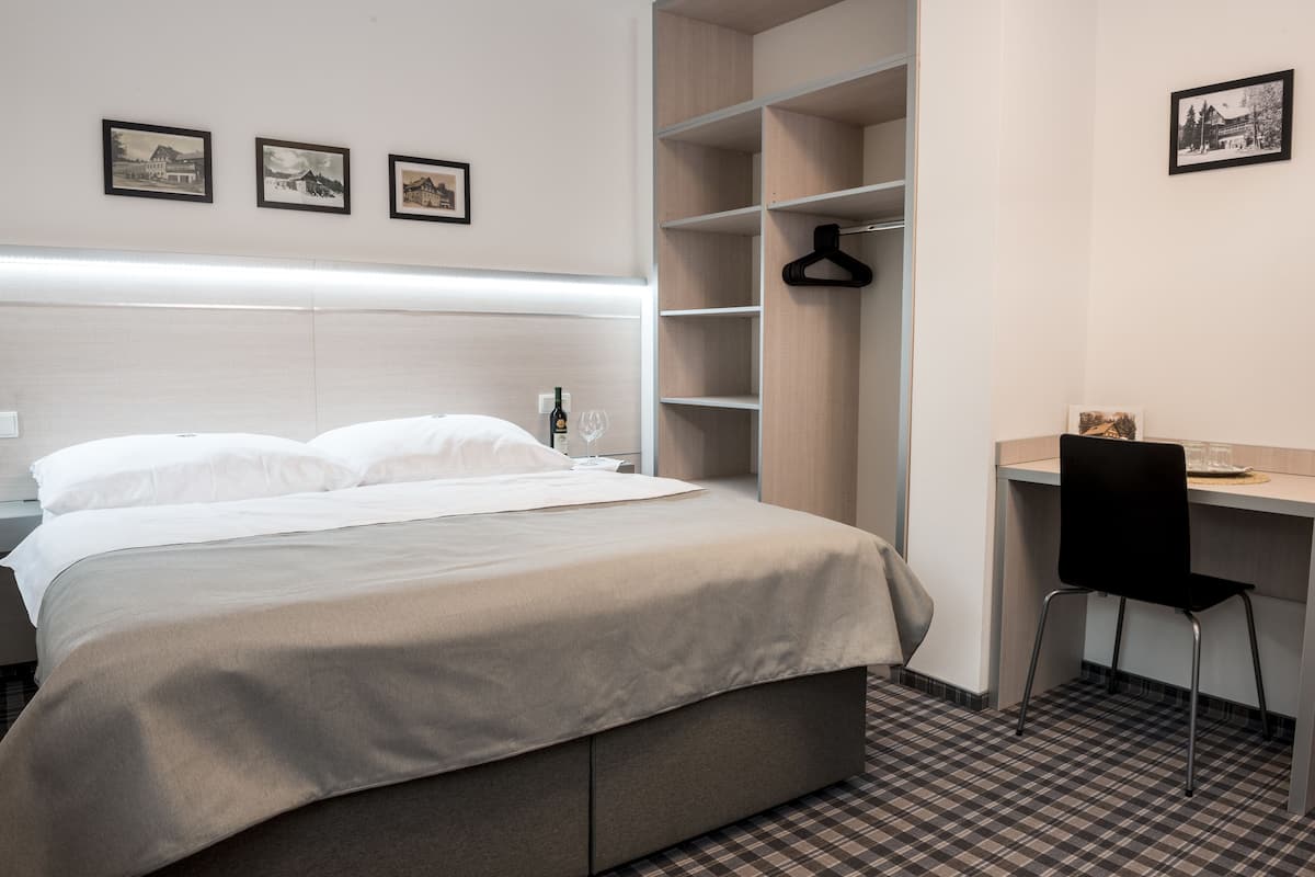 A hotel room with a bed, a desk, and a chair. There are three framed pictures on the wall.