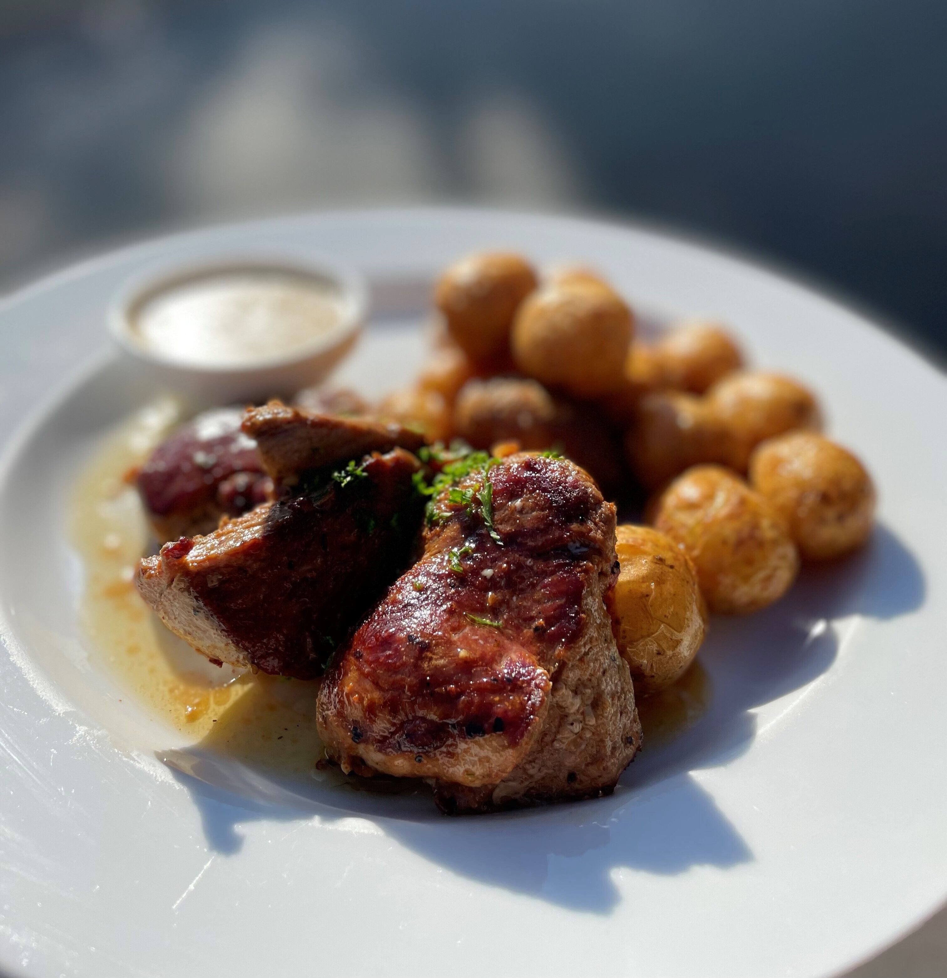A plate with grilled meat, roasted potatoes, and a small bowl of sauce.