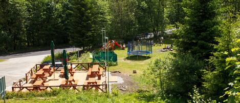 A picnic area with tables and benches, surrounded by trees and a playground.