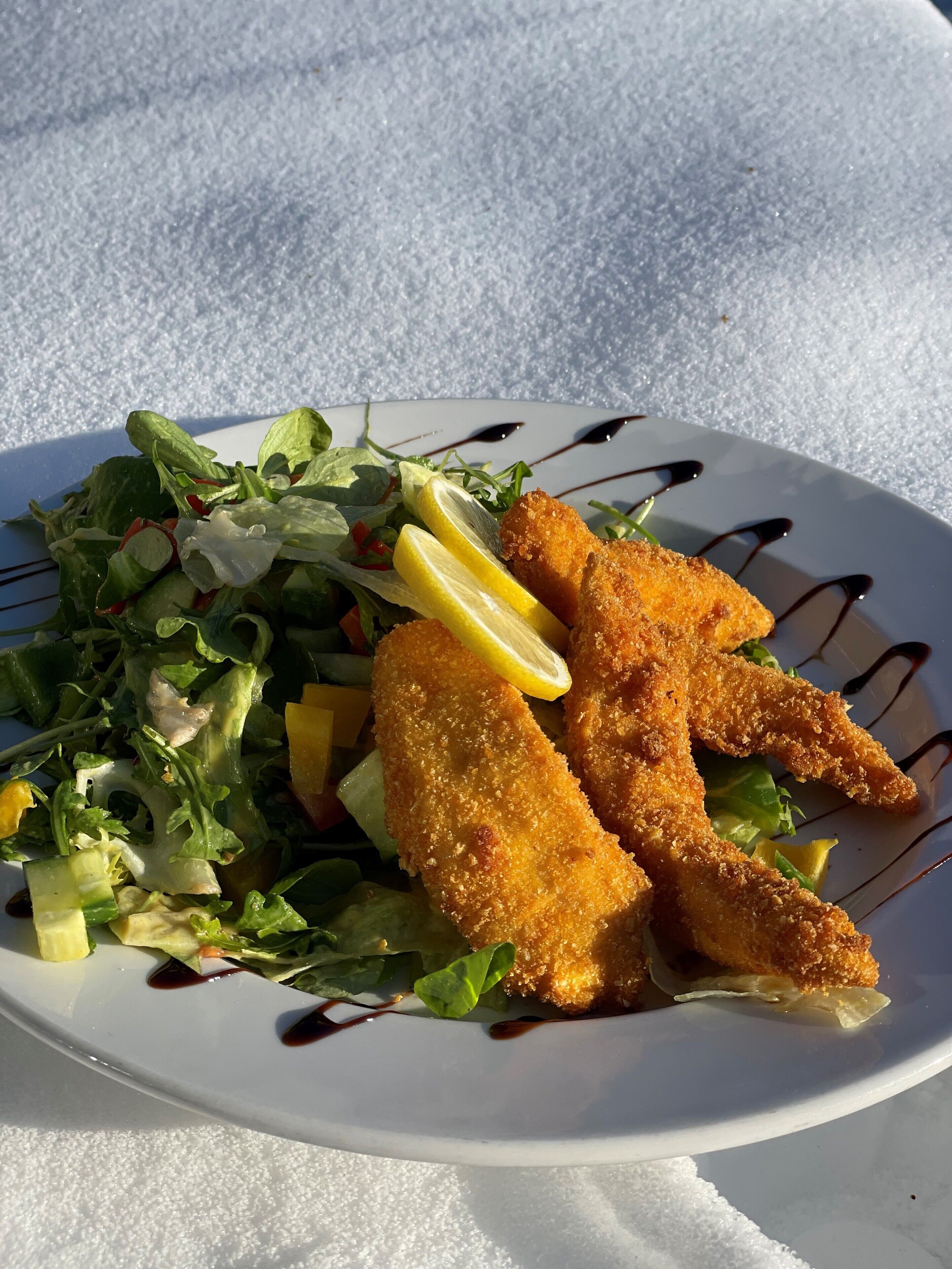 Ein Teller Essen mit Salat und Zitronenscheiben, mit einem Soßenüberzug.