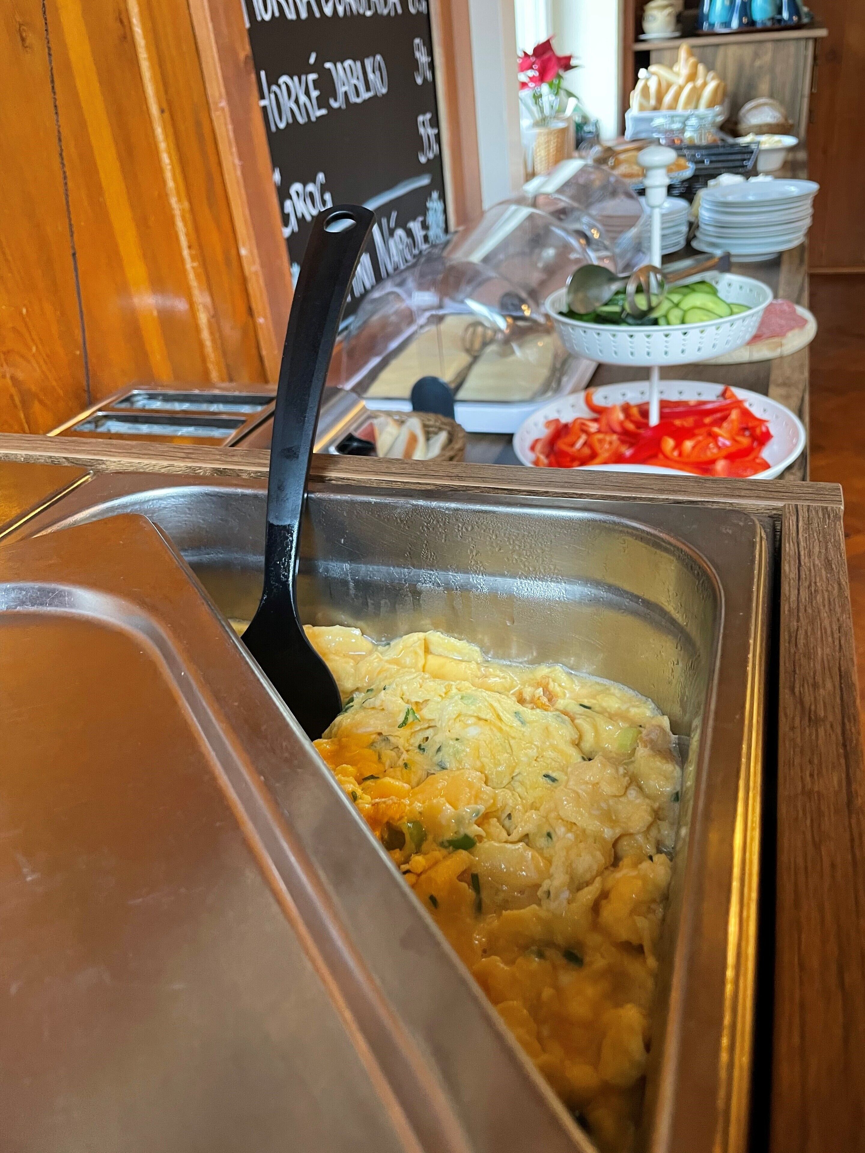 A buffet with a variety of food items including scrambled eggs, vegetables, and bread.
